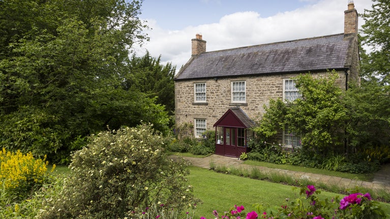Cherryburn farmhouse with lawn in front and framed by trees and plants